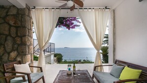 A balcony with a stone wall, a wooden table with a bottle and glasses, and two wooden chairs with cushions. - Villa Mirjana - Studio Apartment with Terrace and Sea View (Bogumila) (Mlini)