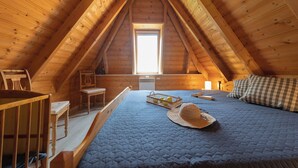 A cozy attic bedroom with a sloped ceiling, a wooden bed, a small desk, and a window providing natural light.