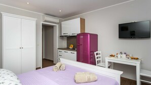 A hotel room with a bed, a desk, a television, a wardrobe, and a kitchenette. - Villa Mirjana - Standard Studio Apartment with Terrace and Sea View (Lavanda) (Mlini)