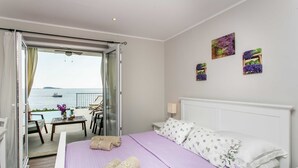 A hotel room with a bed, a view of the sea, and a balcony with a table and chairs. - Villa Mirjana - Standard Studio Apartment with Terrace and Sea View (Lavanda) (Mlini)