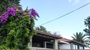 A house with a stone wall and a tiled roof, surrounded by lush greenery and purple flowers. - Villa Mirjana - Standard Studio Apartment with Terrace and Sea View (Lavanda) (Mlini)