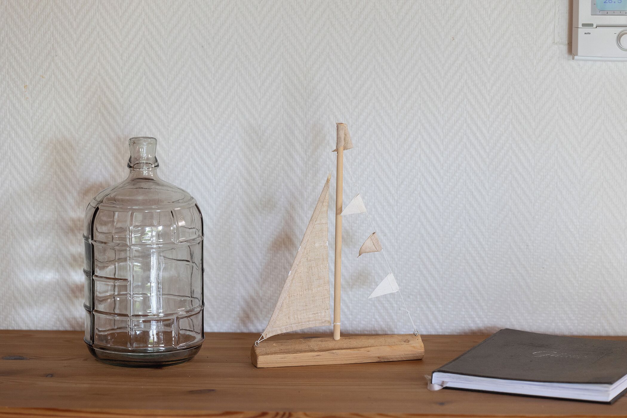 Una botella de vidrio transparente, un modelo de velero de madera y una libreta sobre una superficie de madera.