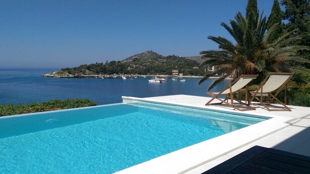A swimming pool with a view of the sea and a hill.