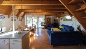Amplia sala de estar con techo alto, vigas de madera, un sofá azul y una mesa de comedor con sillas.