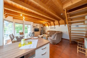 Un vaste espace de vie doté d’un plafond en bois, d’une cheminée, d’un téléviseur et d’un coin repas avec des chaises et une table.