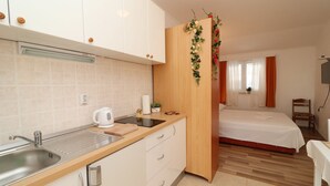 Een compacte hotelkamer met kitchenette, een bed, een tafeltje en een stoel.