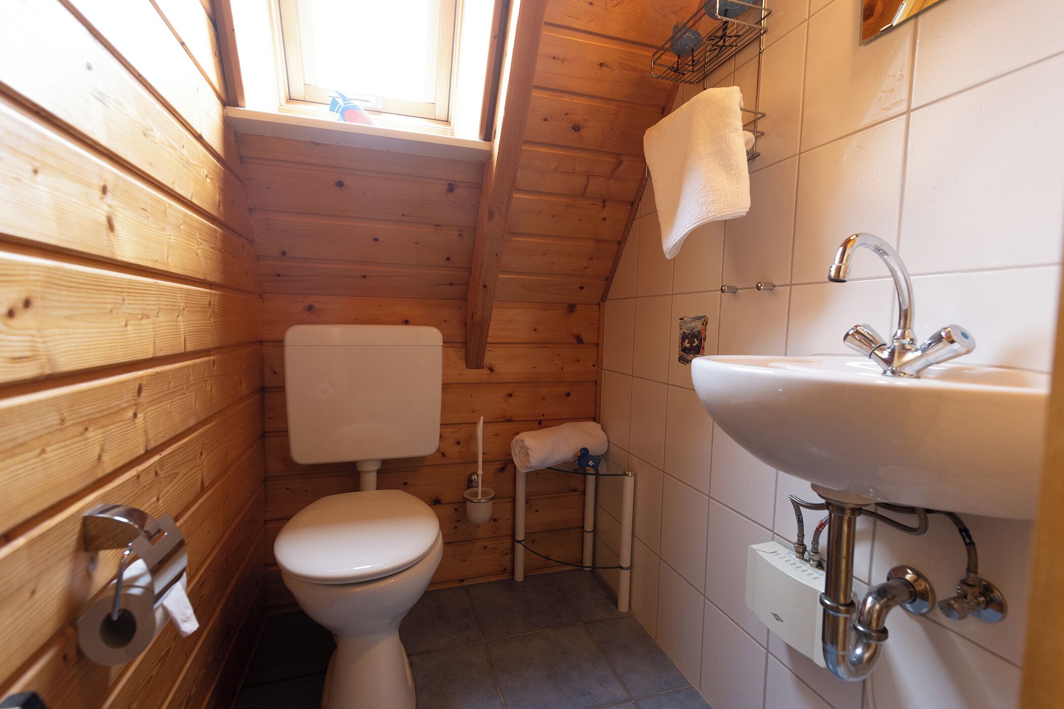 A small, wooden-paneled bathroom with a toilet, sink, and window.