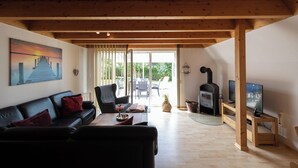 A living room with a wooden ceiling, a black leather sofa, a television, and a fireplace.