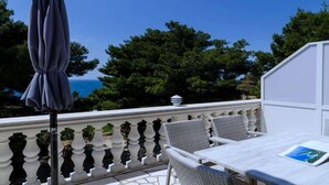 Een balkon met een witte balustrade, rieten stoelen, een tafel en een donkere parasol.