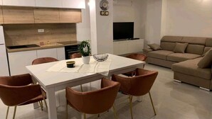 Een moderne woonkamer met een bank, een eettafel met stoelen, en een keukenhoek met kasten en een televisie.