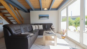Ein modernes Wohnzimmer mit einem Ecksofa, einem Holztisch und Blick ins Freie durch große Fenster.
