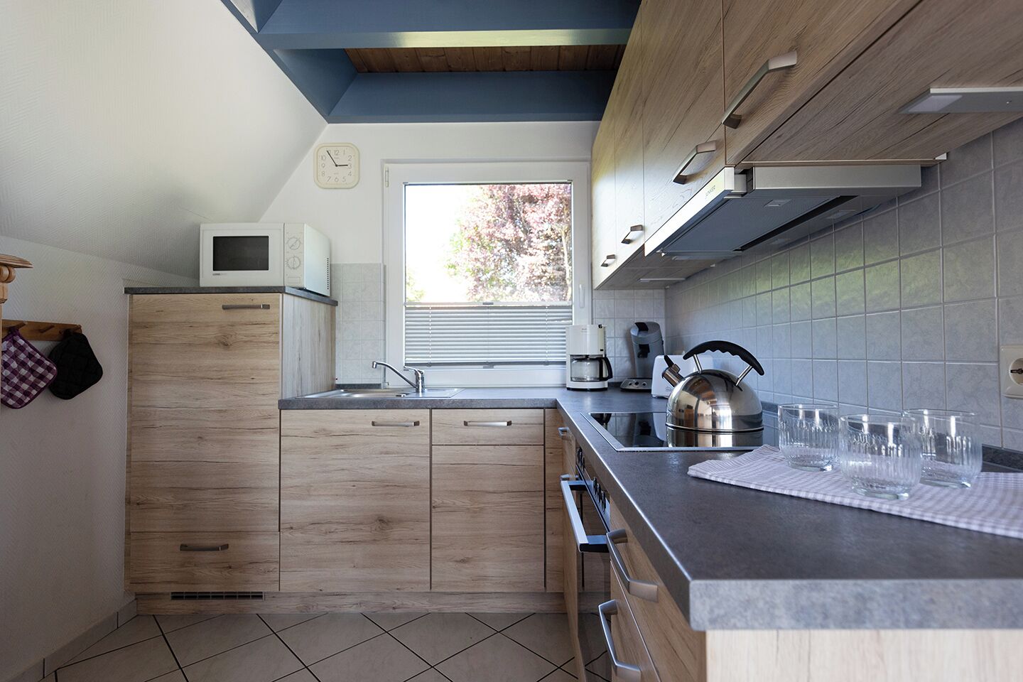 Una cocina moderna con armarios de madera, microondas integrado, hervidor y cafetera.