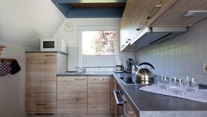 Eine moderne Küche mit Holzschränken, einer eingebauten Mikrowelle, einem Wasserkocher und einer Kaffeemaschine.