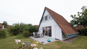 Une maison avec un toit en pente, une terrasse avec des meubles d’extérieur et un petit espace de jeux.