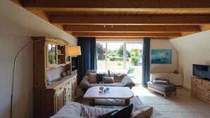 Una sala de estar acogedora con techo de madera, un sofá, una mesita de centro, un televisor y una ventana con cortinas.