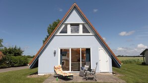 Una casa moderna con techo triangular, puerta corrediza de vidrio y un patio con dos sillas.