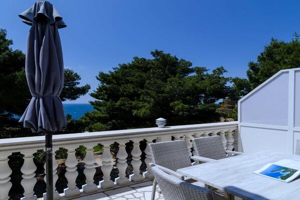 A balcony with a table and chairs, overlooking a body of water and trees.