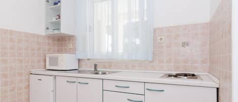 Een kleine keuken met een magnetron, spoelbak en kastjes.