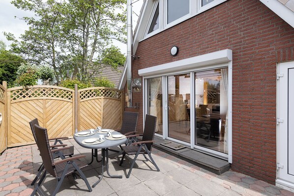 A patio with a table and chairs, a wooden fence, and a brick building with a sliding glass door.