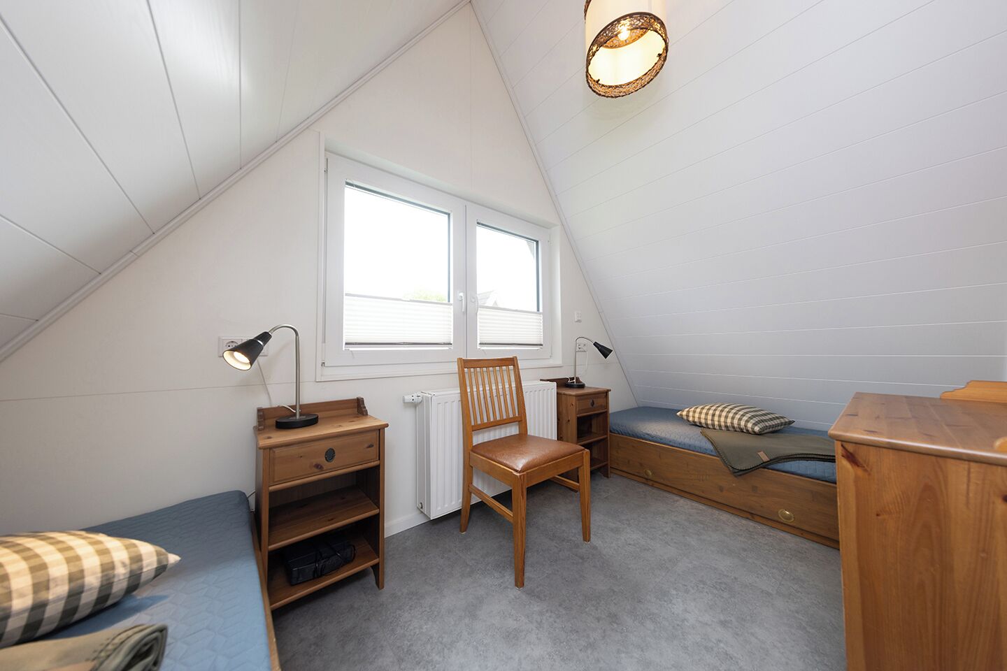 A small, sloped-roof attic bedroom with a desk, chair, and bunk bed.