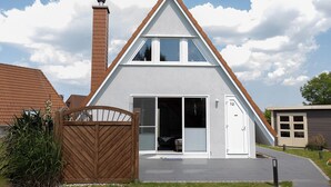 A modern two-story house with a triangular roof, a visible chimney, and a gated entrance. - Vacation home Ebb & Flow. Bright and tasteful. (Wurster Nordseeküste)
