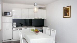 A modern kitchen with white cabinetry, a dining table with chairs, a fruit bowl, and a hanging light fixture.