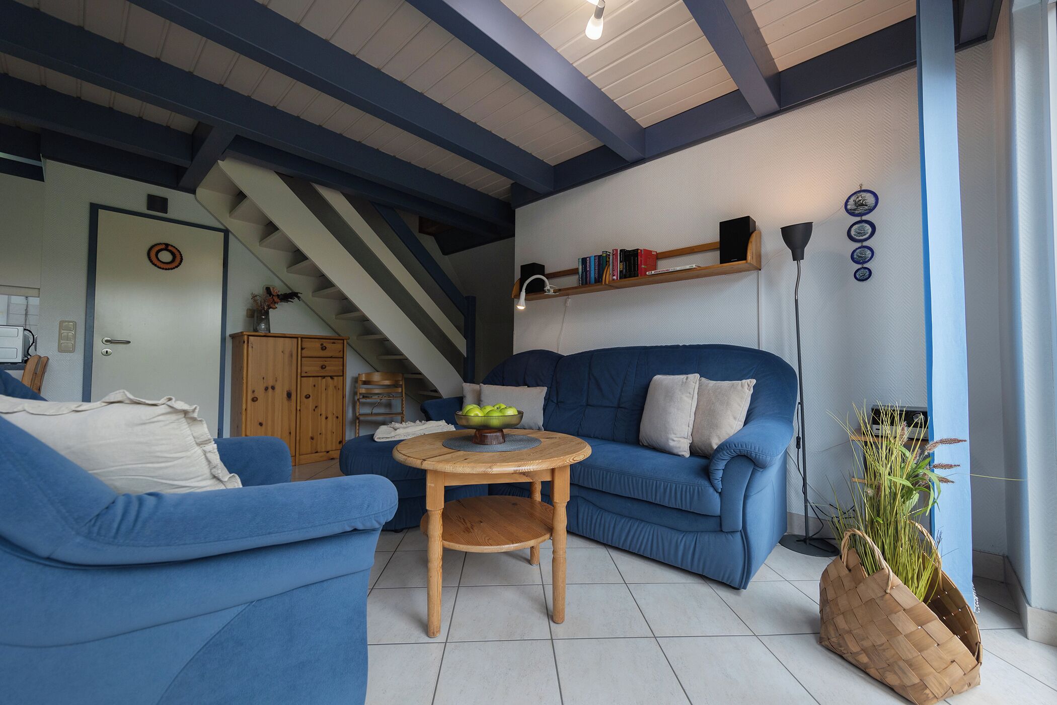 En stue med en blå sofa, et træbord og en trappe i baggrunden.