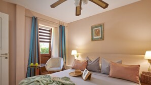 Ein Hotelzimmer mit einem Bett, einem Sessel, einem Tisch mit Früchten, einer Lampe und einem Fenster mit Vorhängen.