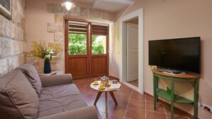 Ein gemütliches Wohnzimmer mit einer Couch, einem Couchtisch mit einem Buch, einem Fernseher auf einem Schrank und einer Steinwand.