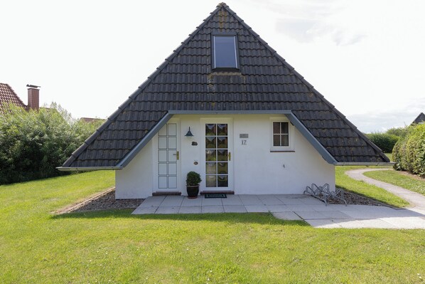 Ett hus med ett brant tak, en liten veranda och en krukväxt.