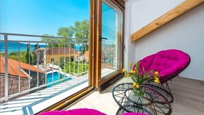 A balcony with a glass door, a round glass table with a vase of flowers, and a bright pink chair. - Villa Mia -Three-Bedroom Villa with Swimming Pool (Trsteno)