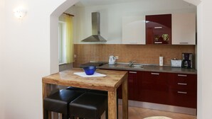 Une cuisine compacte avec une table en bois, deux chaises noires, une cuisinière encastrée, un évier et des placards rouges.