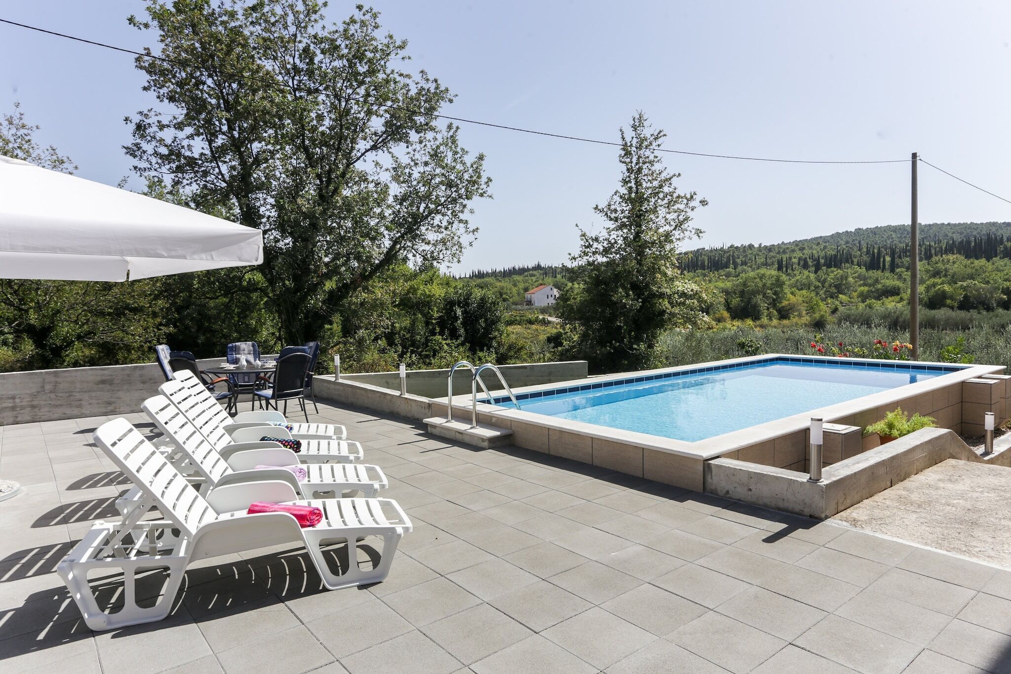 Un espace piscine aménagé sur le toit, avec des chaises longues et une table, entouré d’arbres et offrant une vue sur la campagne.