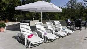 Une terrasse avec des chaises longues blanches, un parasol blanc et un barbecue.