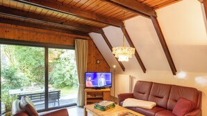 A cozy living room with a television, leather sofa, wooden coffee table, and a view of the outdoors. - Vacation home Robbenplate 11, flooded with light and close to the cutter harbor. (Wurster Nordseeküste)
