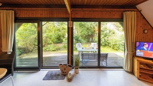 A wooden interior with a large sliding glass door leading to an outdoor deck. Inside, there is a television, a plant, and a small table with chairs. - Vacation home Robbenplate 11, flooded with light and close to the cutter harbor. (Wurster Nordseeküste)
