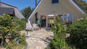 Une maison dotée d’une terrasse en pierre, d’un espace salon extérieur et d’une grande porte vitrée donnant sur une zone abritée.