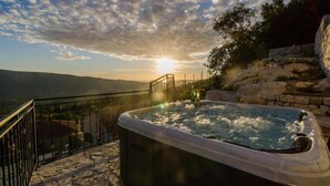 Un jacuzzi en una terraza de piedra con vistas al paisaje y una puesta de sol.
