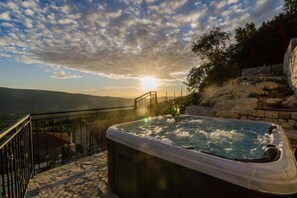 A hot tub on a stone deck with a view of the landscape and a sunset.