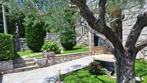 Un sendero de piedra conduce a un edificio con fachada de piedra, rodeado de follaje cuidado y un cielo despejado.