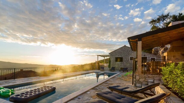 Un área de piscina con sillones de descanso, un edificio de piedra y vistas a las montañas.