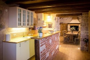 A rustic kitchen with a brick island, wooden beams, and stone walls.