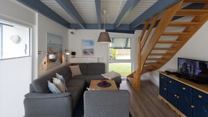 Ein modernes Wohnzimmer mit einem grauen Ecksofa, einem Holztisch und einem Fernseher auf einem blauen Schrank. Im Hintergrund ist eine Holztreppe zu sehen.