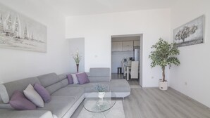 Een moderne woonkamer met een grijze bank, een glazen bijzettafeltje en een potplant.