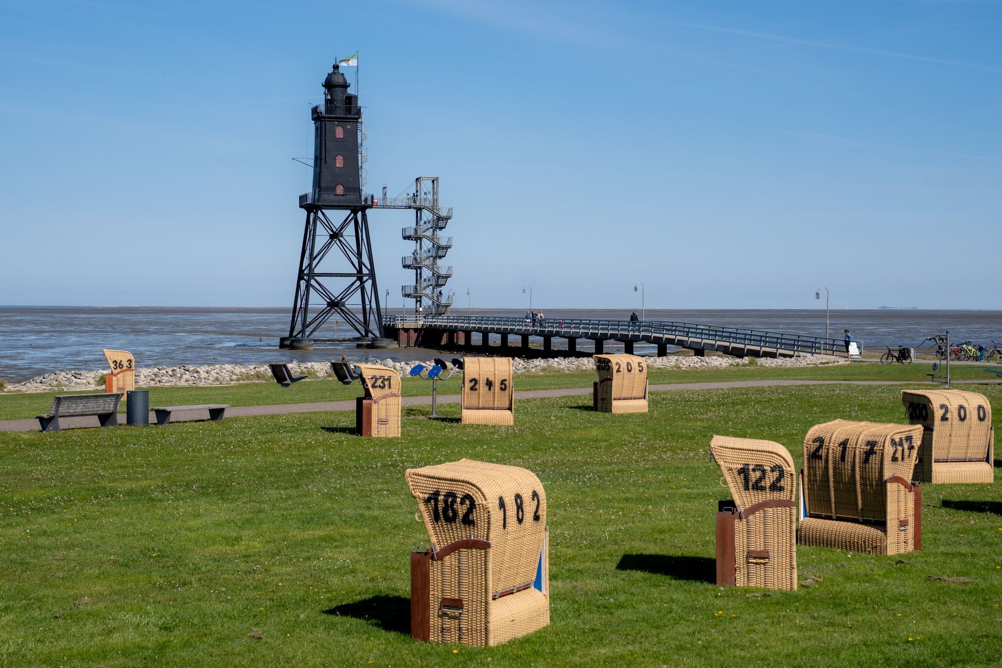 A coastal scene with a lighthouse, a pier, and wicker chairs numbered for an event.