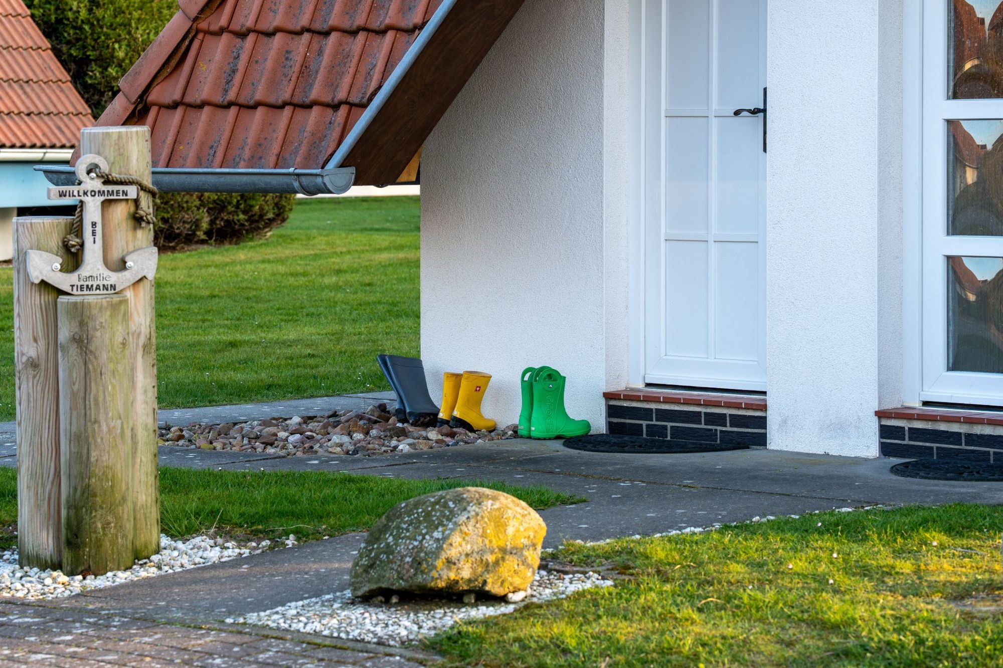 A house with a white exterior, a red-tiled roof, and a wooden post with a welcome sign.