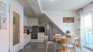 A modern kitchen with white cabinets, a built-in oven, and a refrigerator. There is a dining area with a wooden table and chairs.