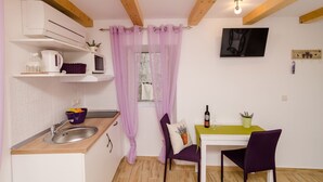 A compact kitchen with a sink, a microwave, and a small window with purple curtains. - Lavender Garden Apartments - Studio Apartment (Ground floor) - APT 1 (Dubrovnik)