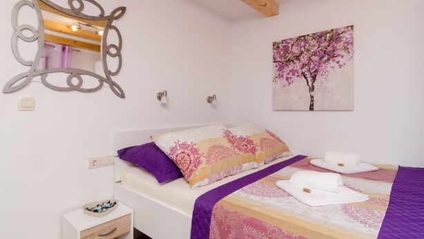 A neatly arranged bedroom with a bed, a heart-shaped bowl on a bedside table, and a wall-mounted mirror. - Lavender Garden Apartments - Studio Apartment (Ground floor) - APT 1 (Dubrovnik)