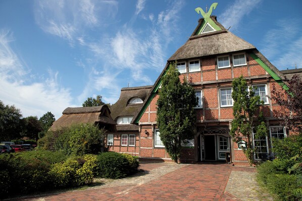 A traditional brick building with a thatched roof and a green cross on top.